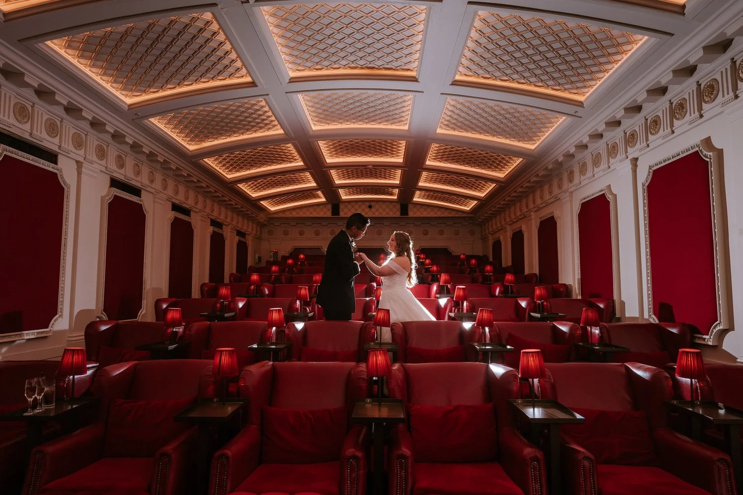 A wide view of Allie and Carl sharing a kiss beneath the ornate ceiling of The Scotsman Picturehouse.