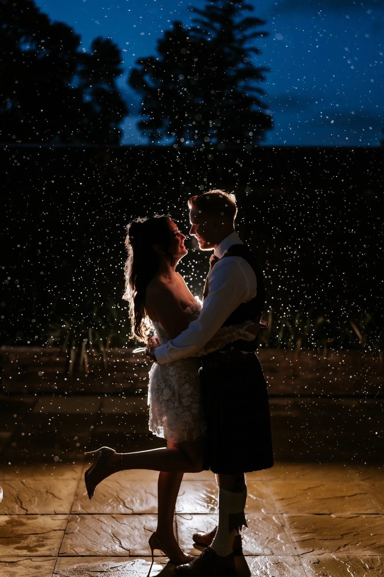 Kaitlyn and Scott embracing in backlit rain on the terrace at night at Glenbervie House.