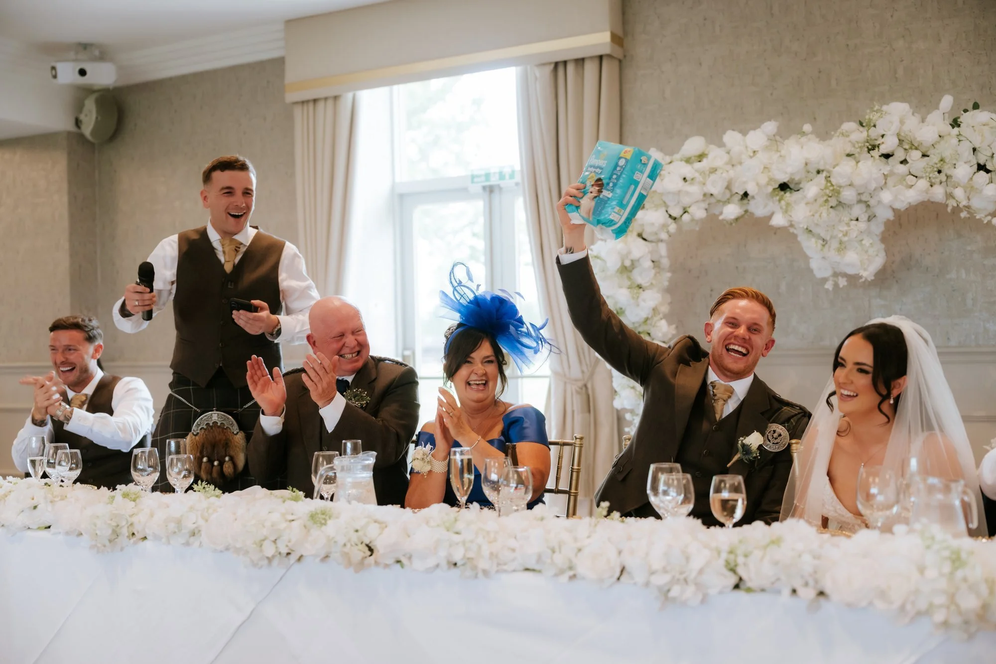 Scott holding up a packet of nappies as the top table laughs during the speeches at Glenbervie House.