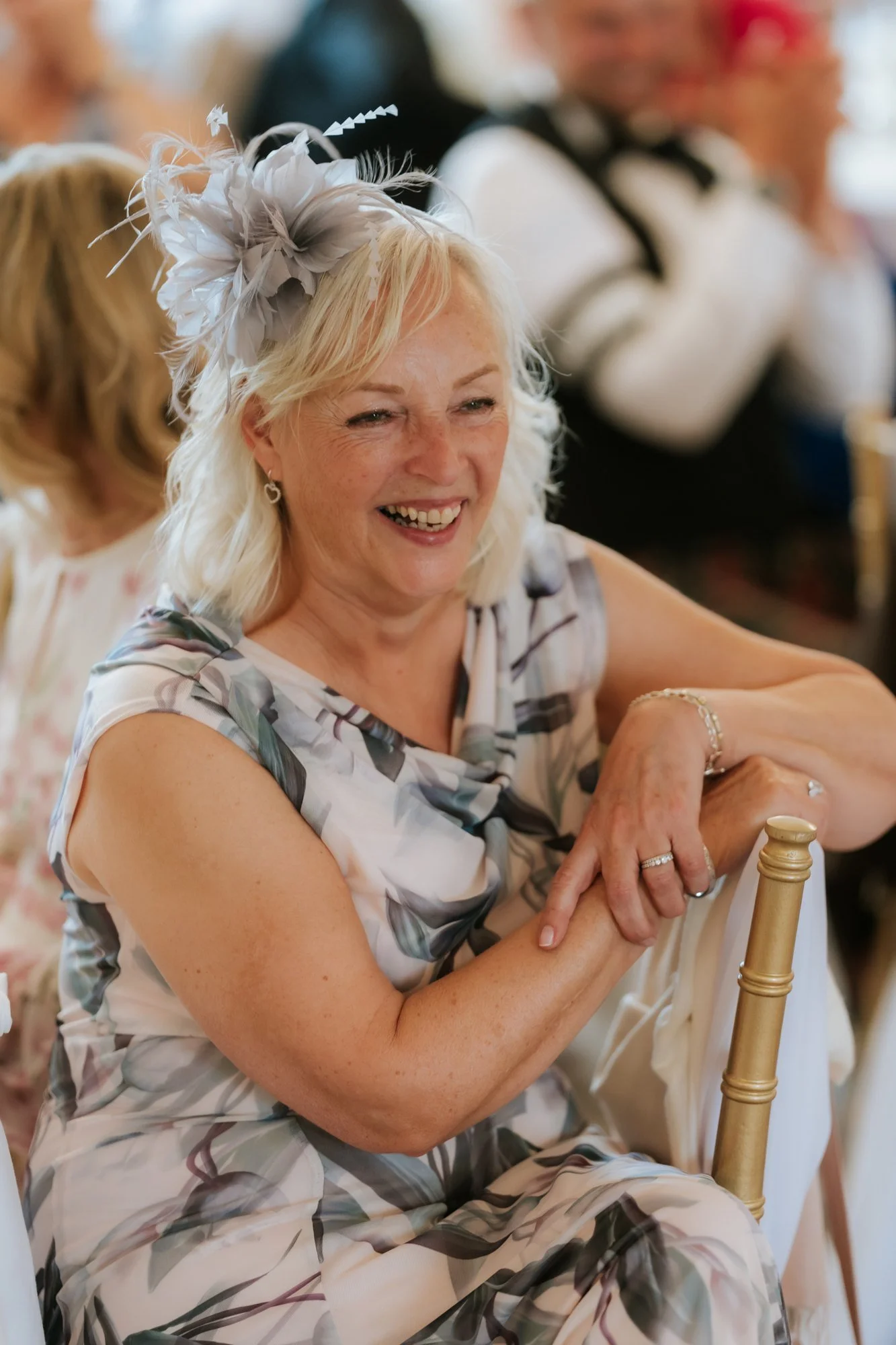 A smiling wedding guest in a floral dress and pale fascinator at Glenbervie House.