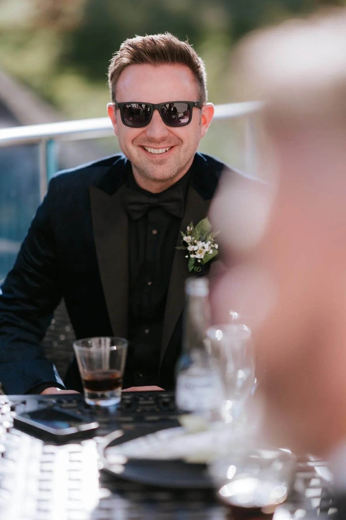 A wedding guest wearing sunglasses and enjoying a drink at the reception.