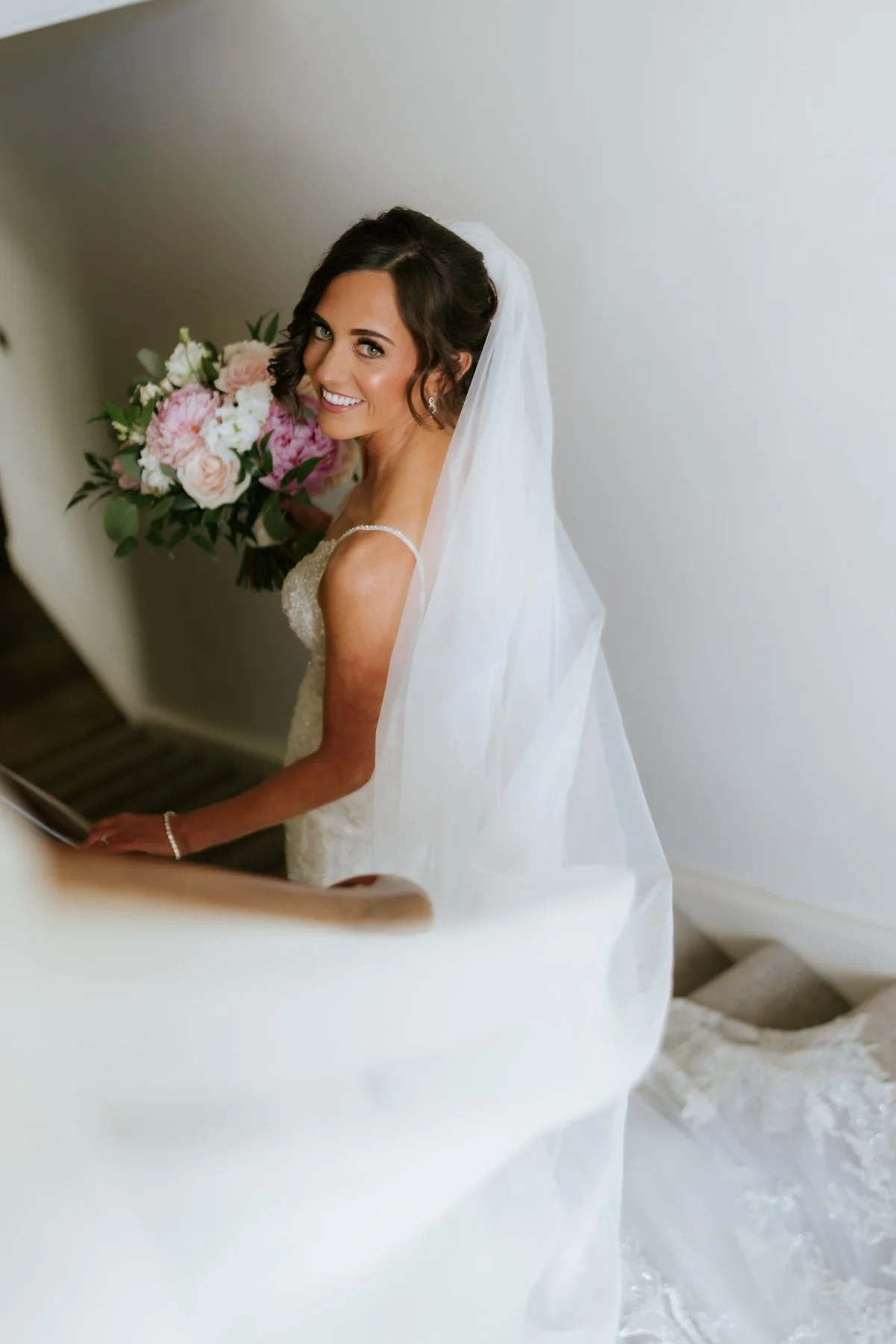 Lauren looking back with her bouquet on the curved staircase while getting ready at Cairns Farm.