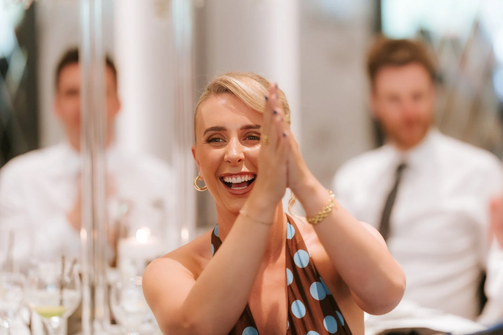 A guest in a blue spotted dress clapping above her head