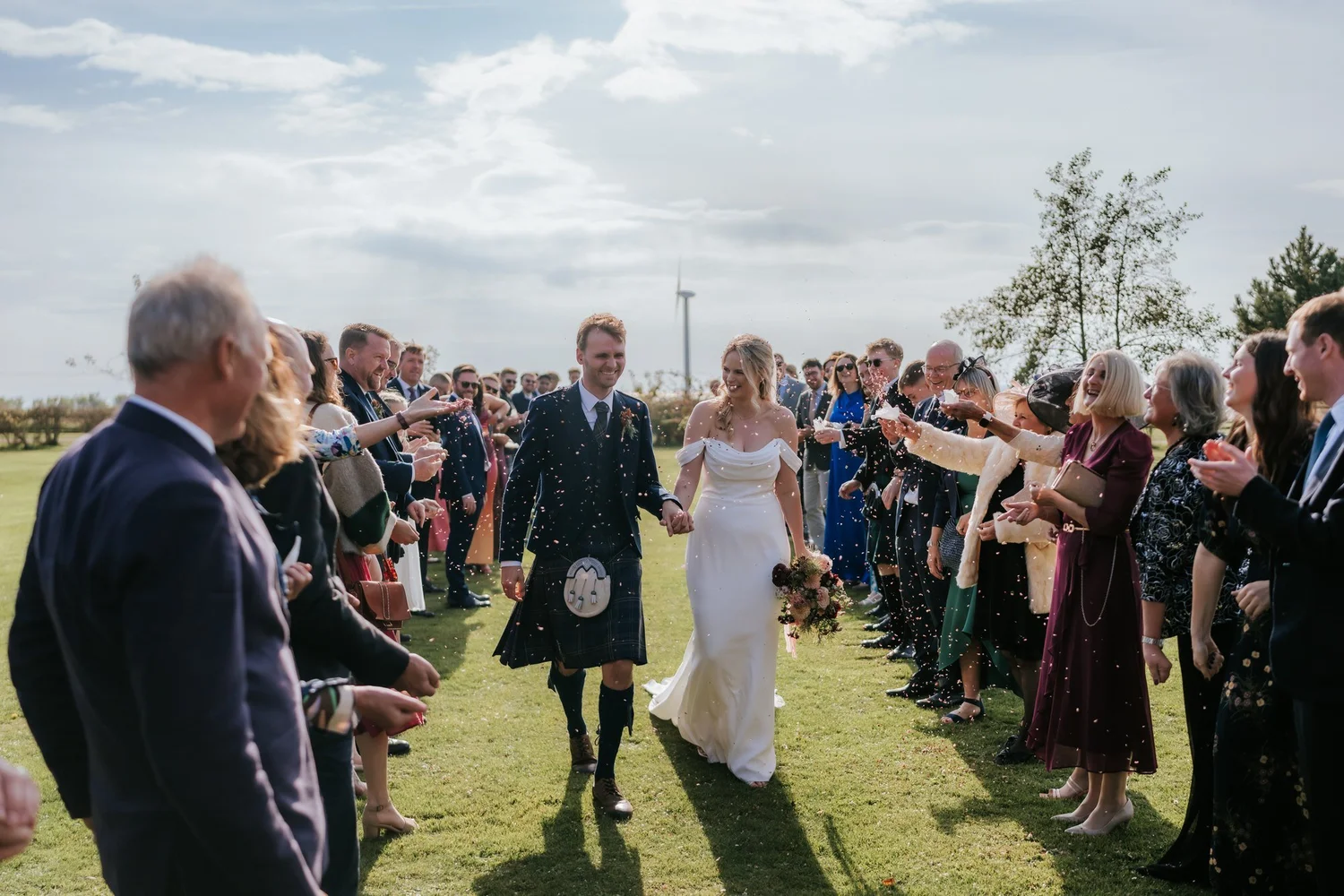 The couple walk between rows of cheering guests as confetti fills the air after the ceremony.