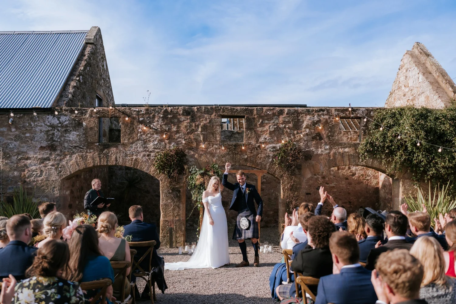 A wide view of the couple standing before their seated guests during the outdoor courtyard ceremony.