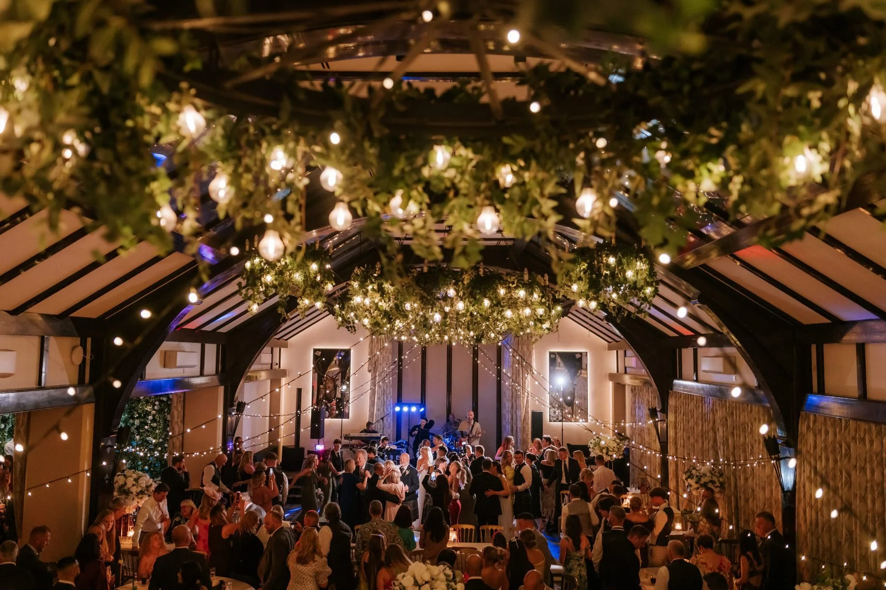 A wide view of the packed dance floor beneath the ballroom’s lights and greenery.