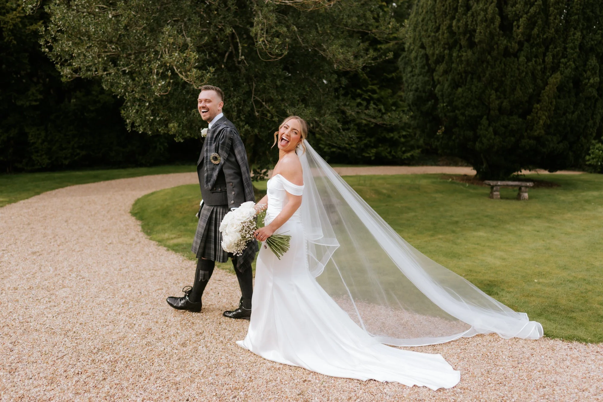 Elle and Adam walking together, smiling back beneath Elle's flowing veil