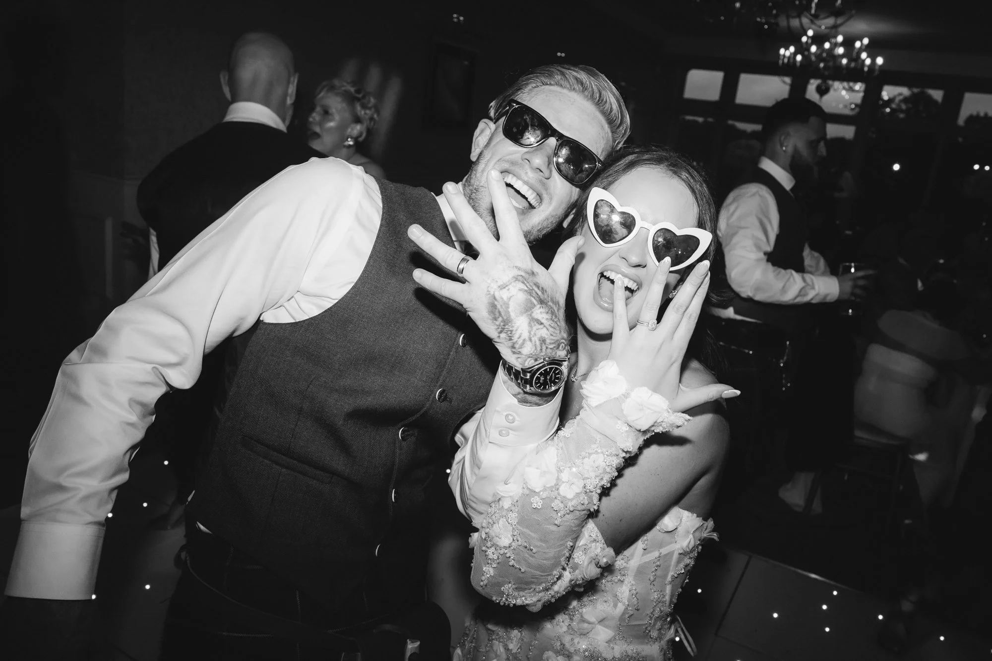 Black-and-white photograph of Kaitlyn and Scott in sunglasses showing their rings at Glenbervie House.