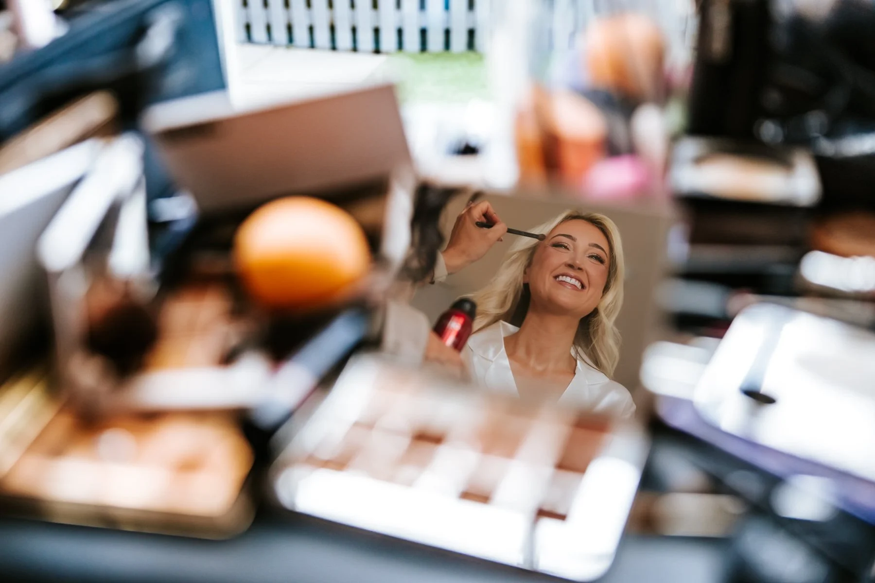 Lauren smiling in a small mirror during her wedding make-up preparations.