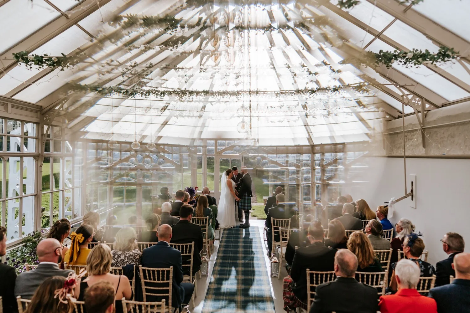 Kendall and Ewen kissing at the front of the sunlit conservatory as their guests applaud.