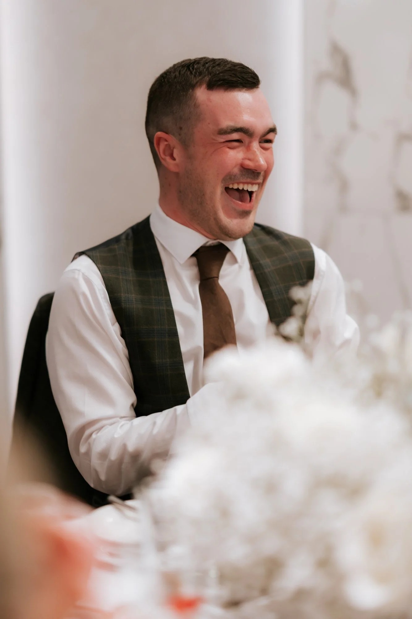 A male guest in a waistcoat laughing at the table