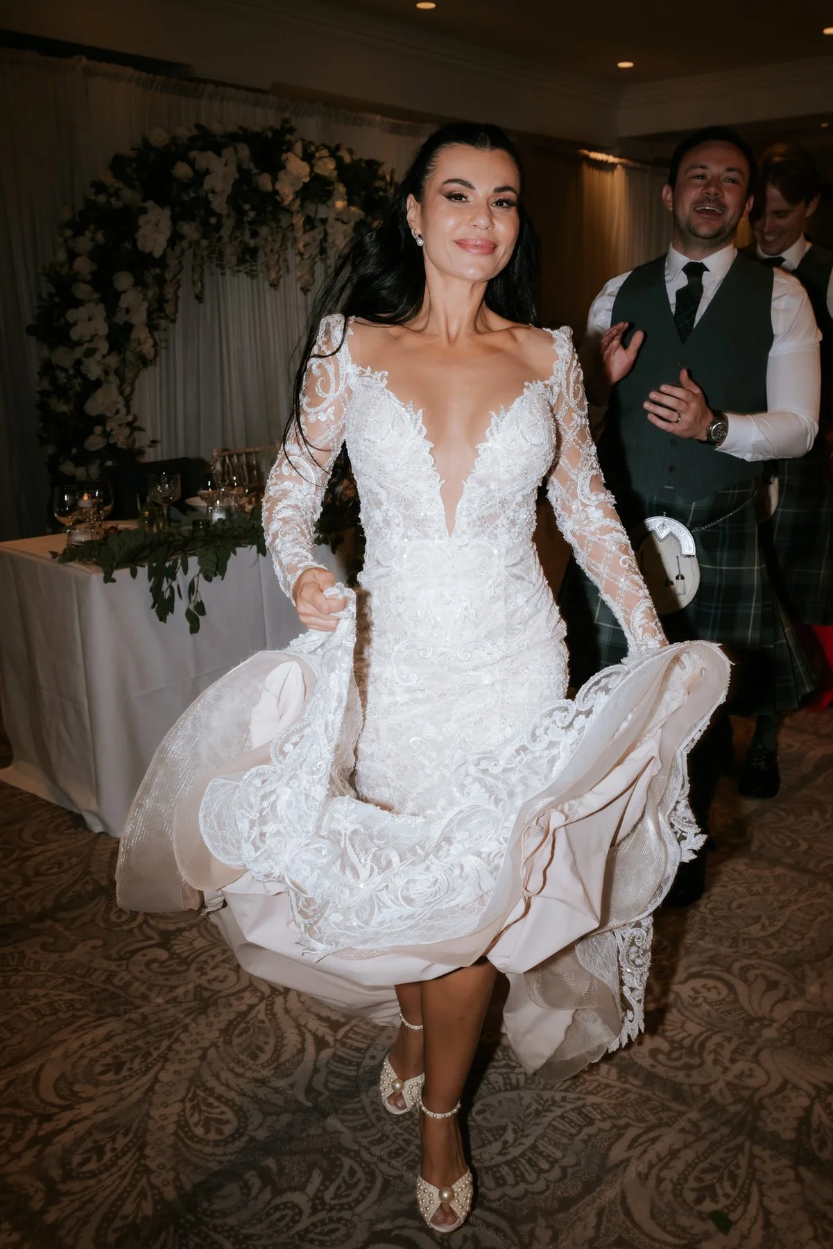 Cristina lifting the hem of her dress and laughing during the reception celebrations, with Connor behind her.