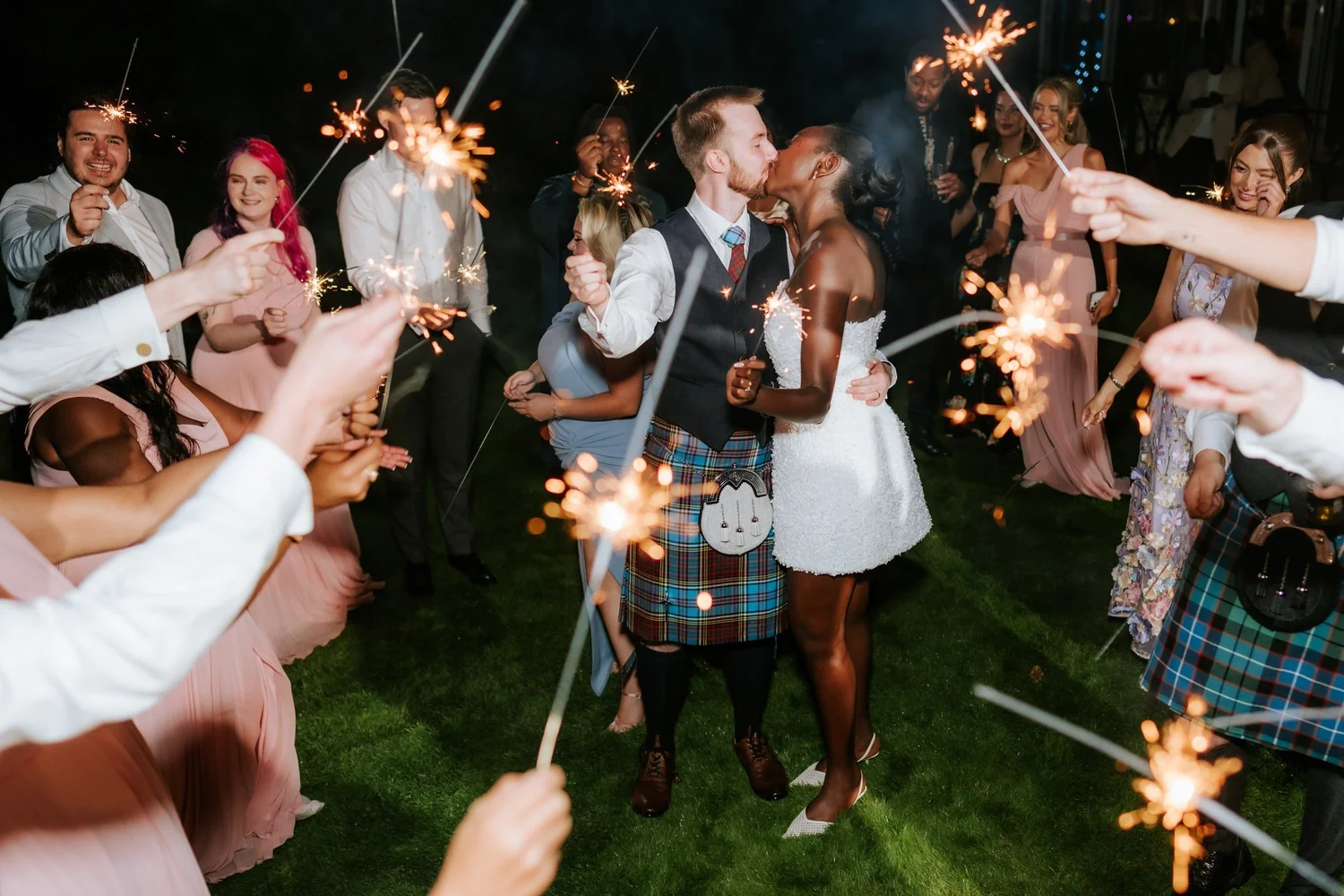 The newlyweds kissing in a circle of sparklers and cheering guests.