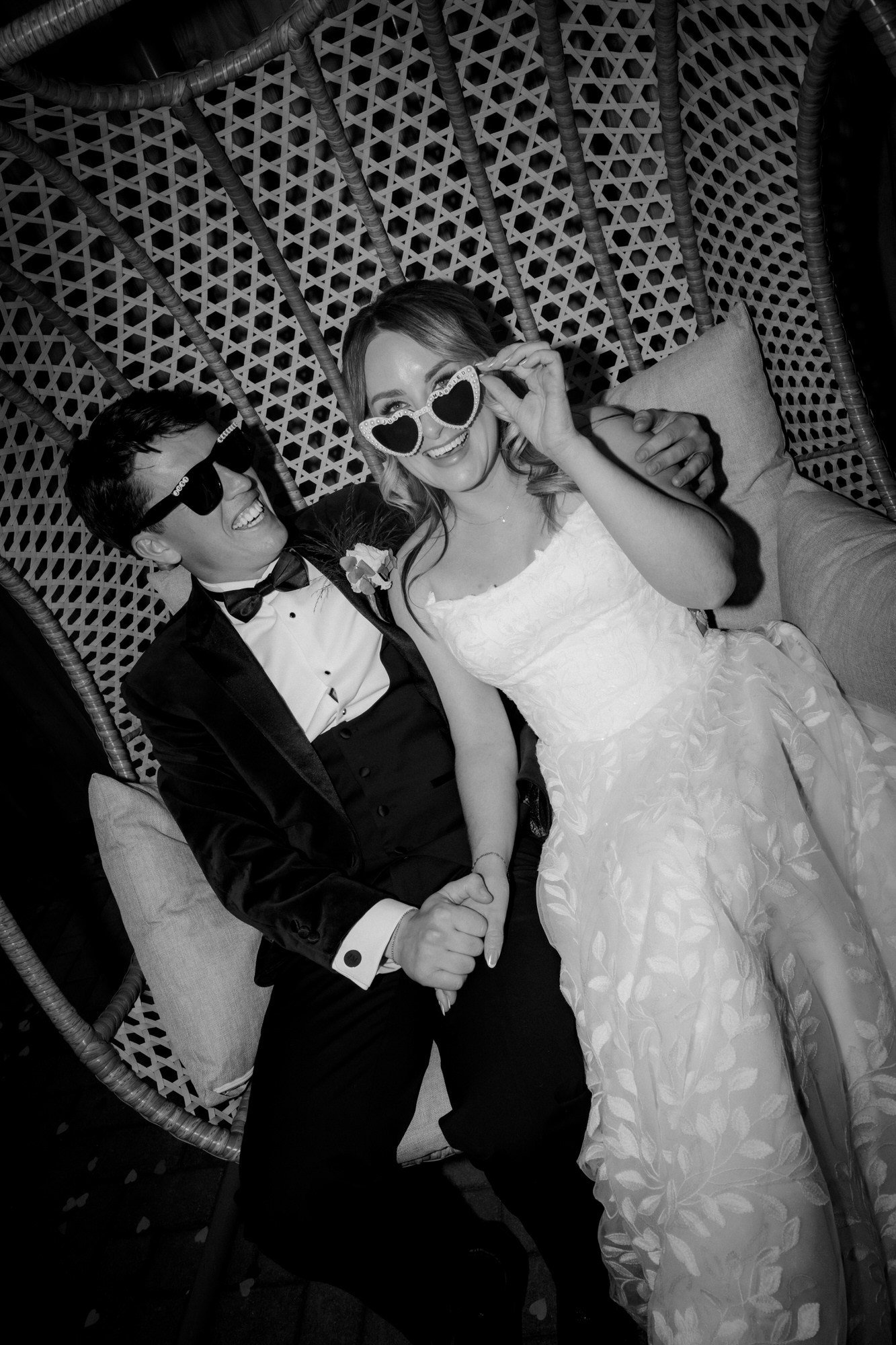 Ciara and Jonathon laughing in a wicker seat wearing wedding sunglasses.
