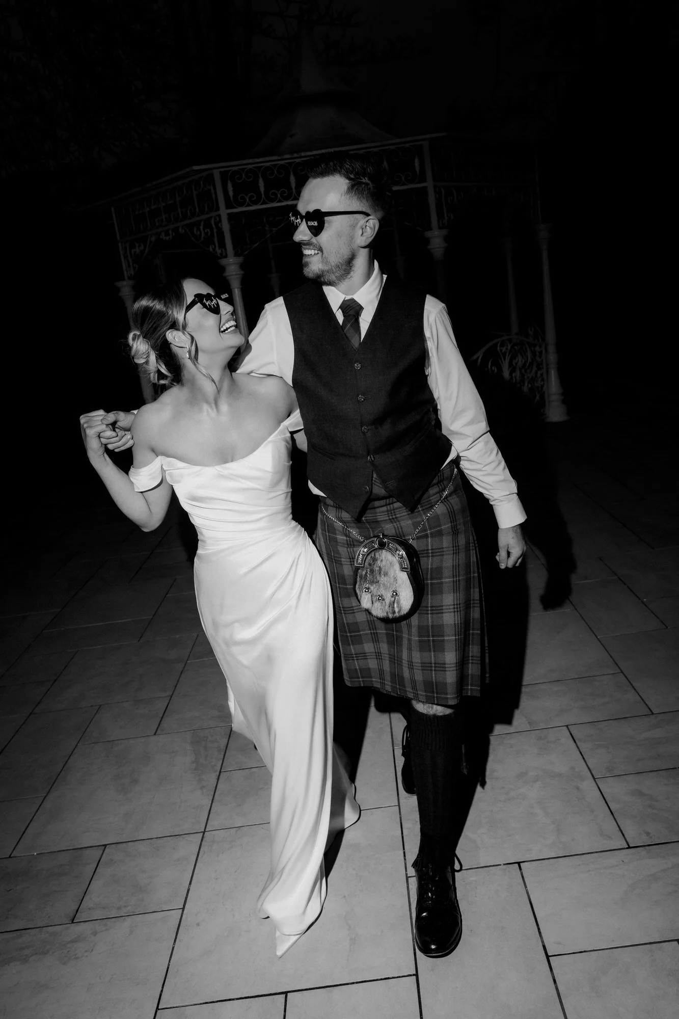 Elle and Adam smiling at each other in heart-shaped sunglasses, in black and white