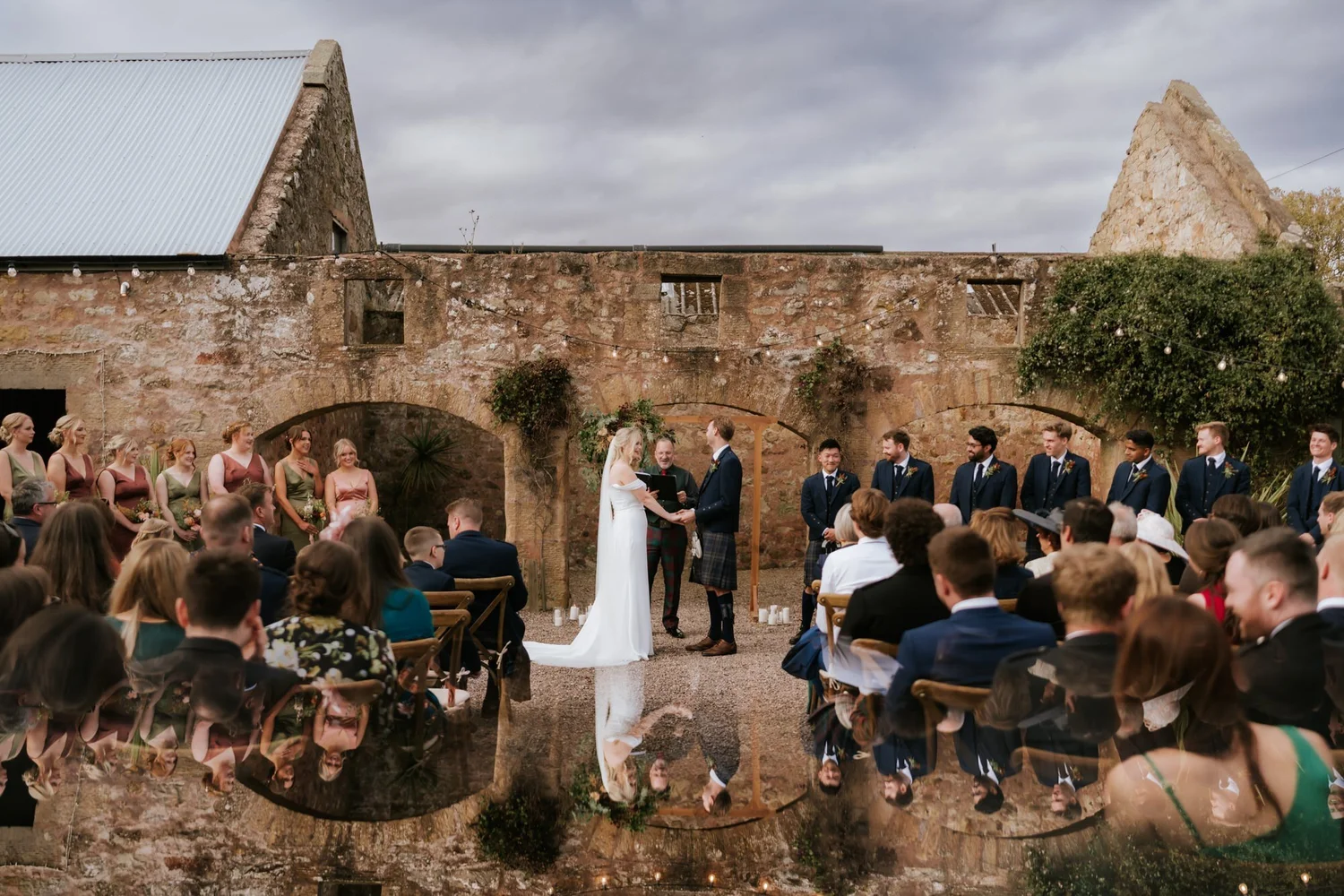 Guests sit facing the couple and celebrant in the stone courtyard at The Cow Shed Crail.