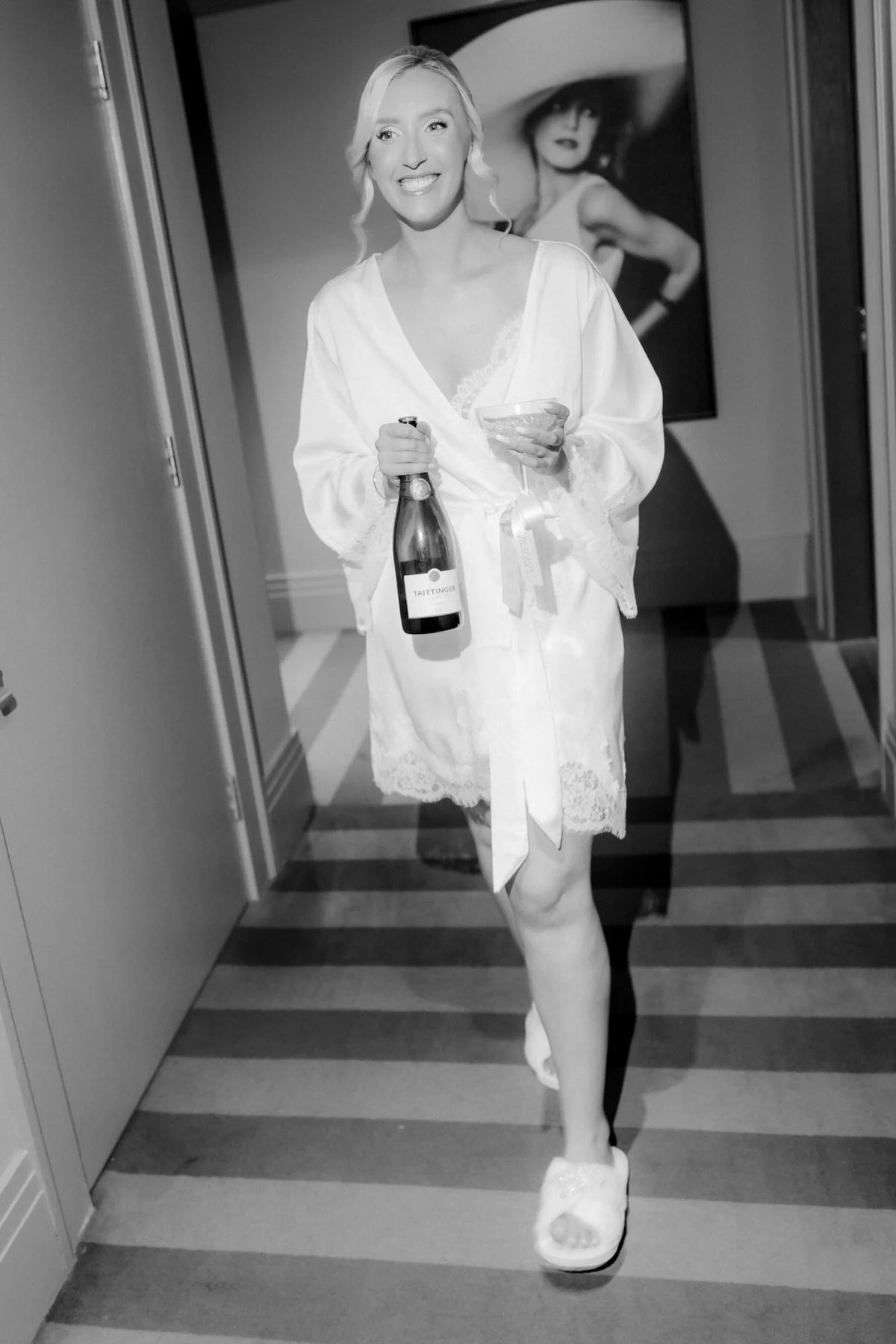 Black-and-white photograph of Jen laughing in her wedding-morning robe with a bottle in her hand.