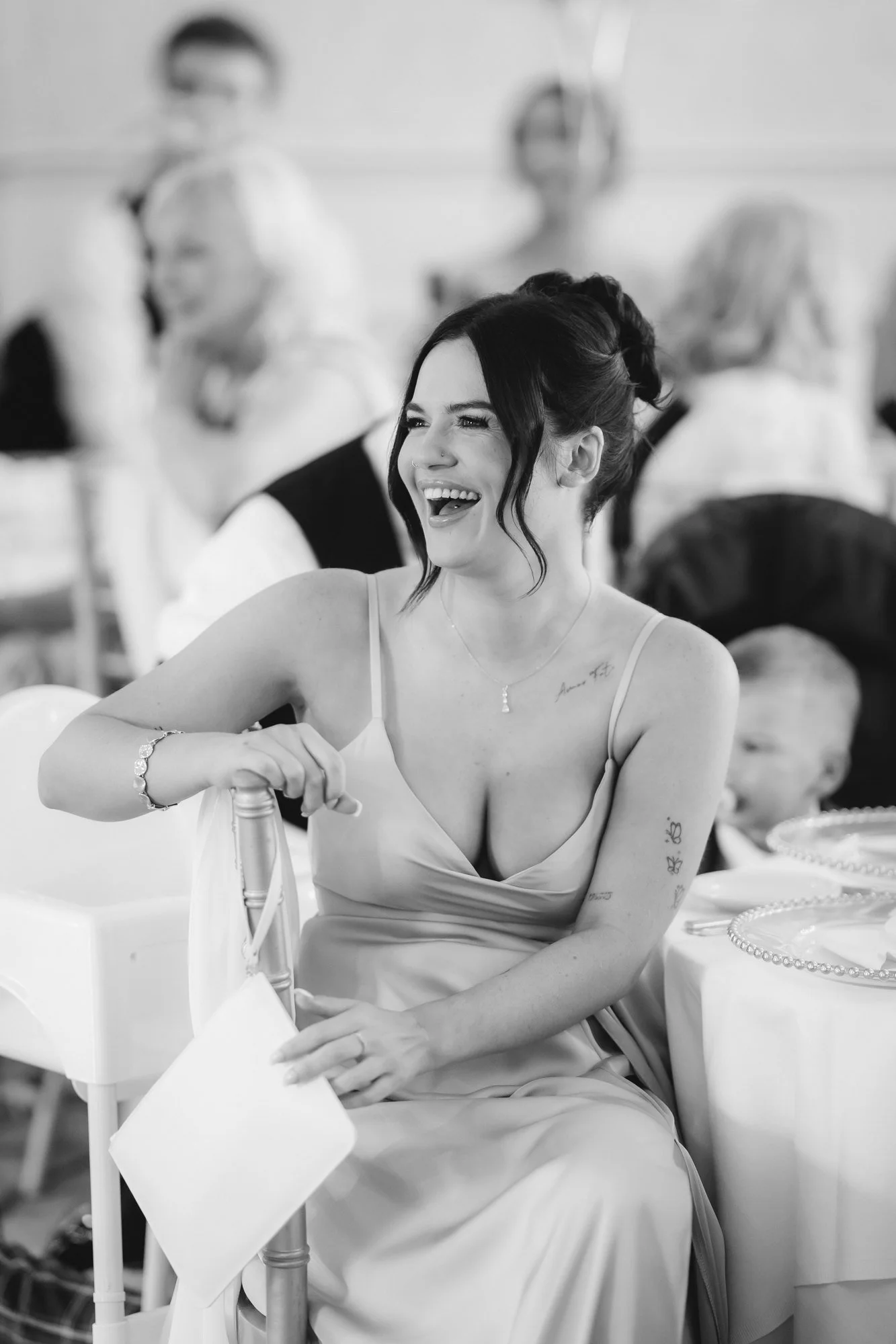 Black-and-white photograph of a bridesmaid laughing with a napkin in her hand at Glenbervie House.