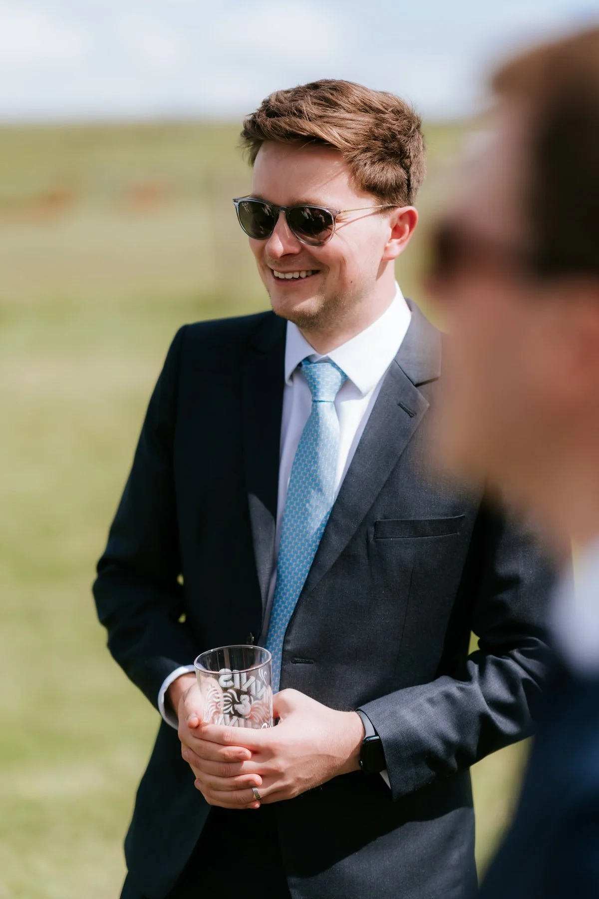 A guest in sunglasses laughing and holding a drink outside.