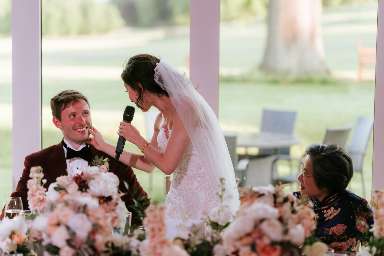 Kim holding a microphone and leaning towards Kenneth as she speaks at their wedding reception.