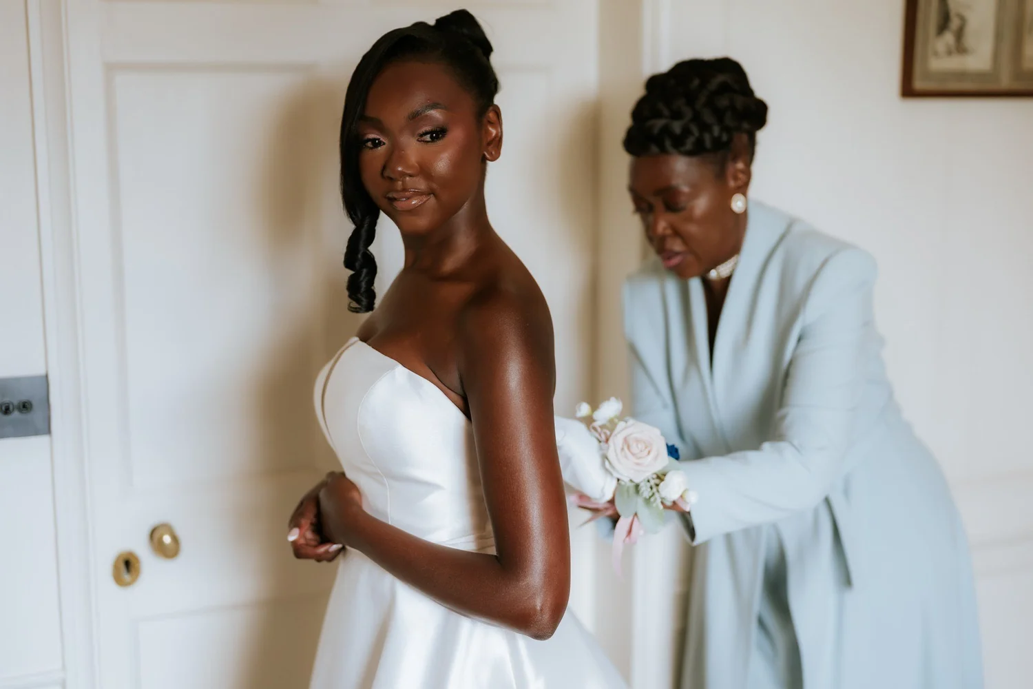 Kuda looking towards the camera as her mum fastens her wedding dress.