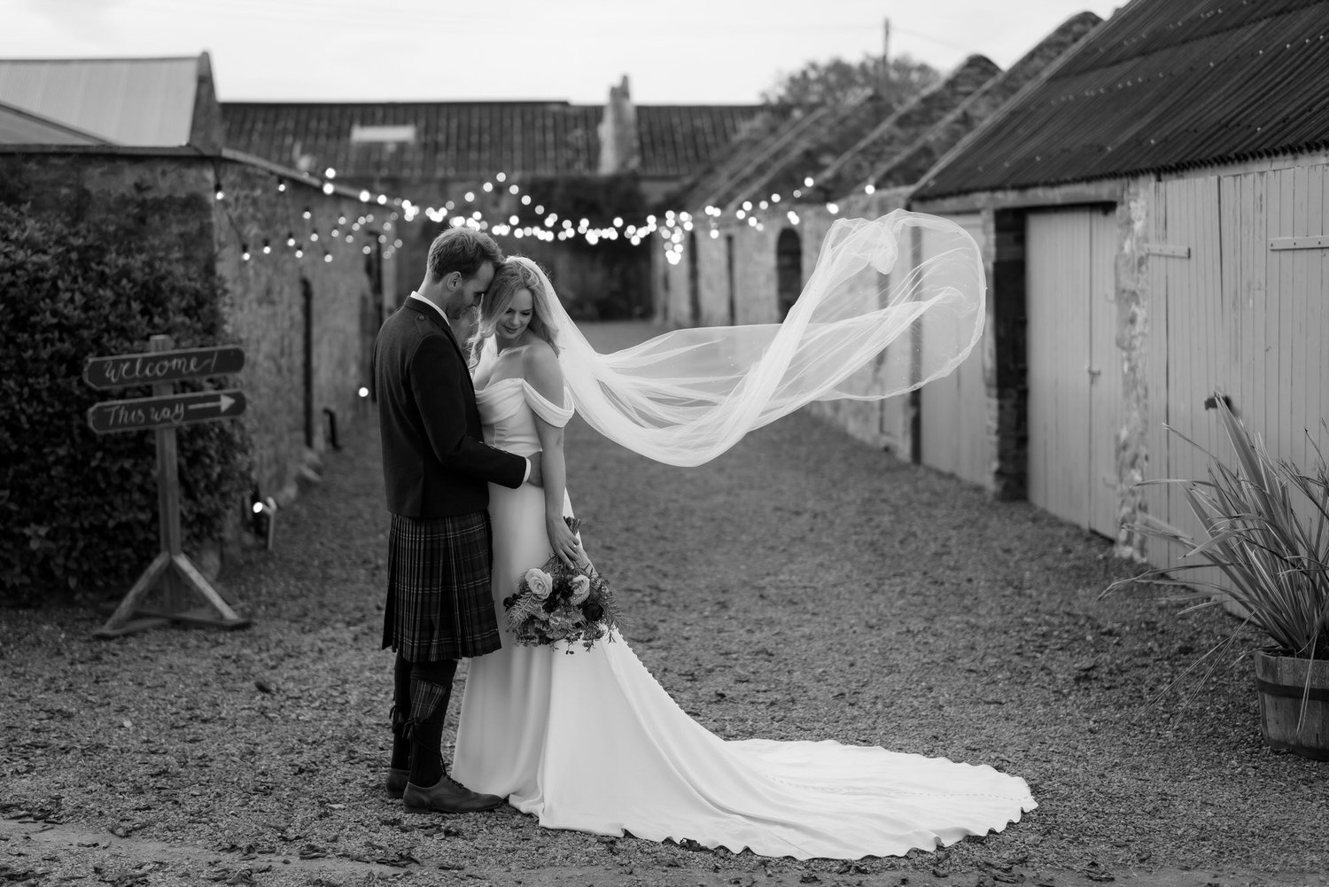 Black-and-white portrait of the couple kissing as the bride’s veil lifts across the courtyard.