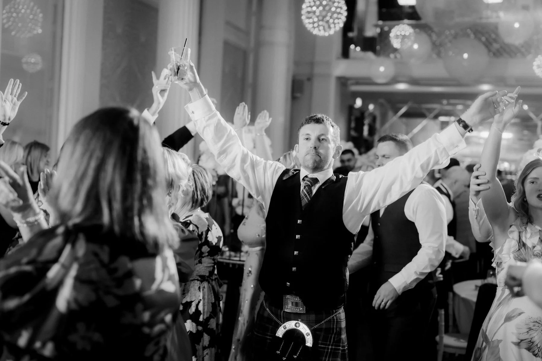 A guest dancing with both arms outstretched among the crowd, photographed in black and white.