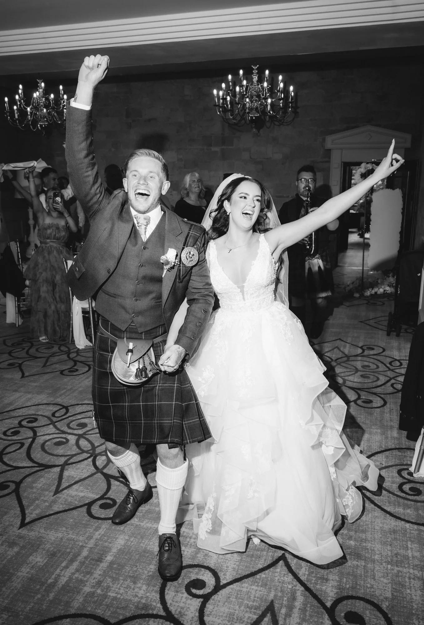 Black-and-white photograph of Kaitlyn and Scott cheering as they enter their reception at Glenbervie House.
