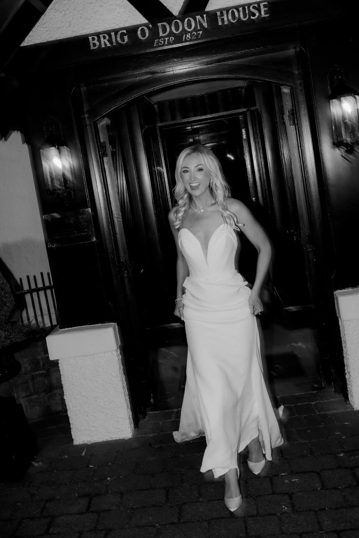 Lauren standing beneath the Brig o’ Doon House sign in an evening black-and-white portrait.