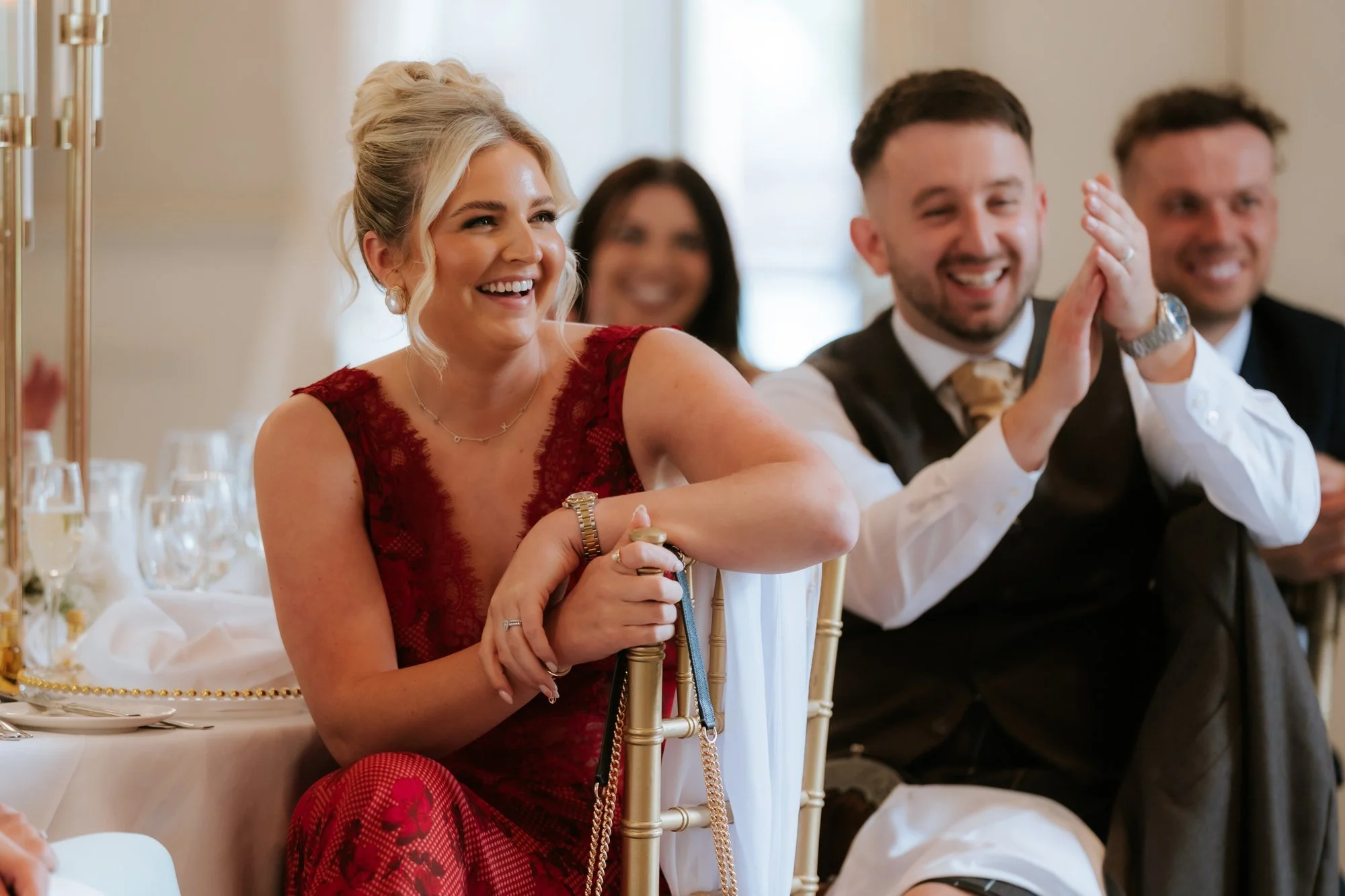A guest in a red dress laughing beside a guest applauding at Glenbervie House.