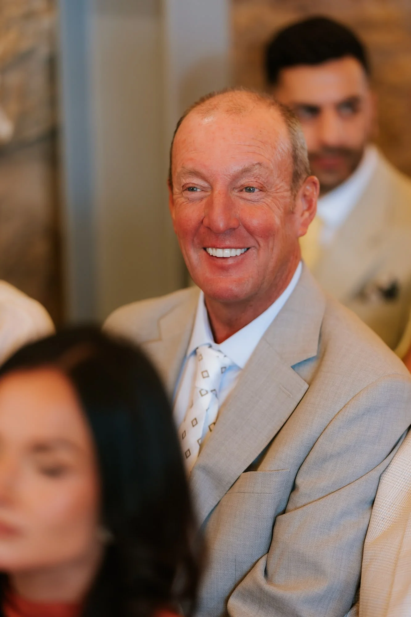 A guest in a grey suit smiling as he watches the wedding ceremony
