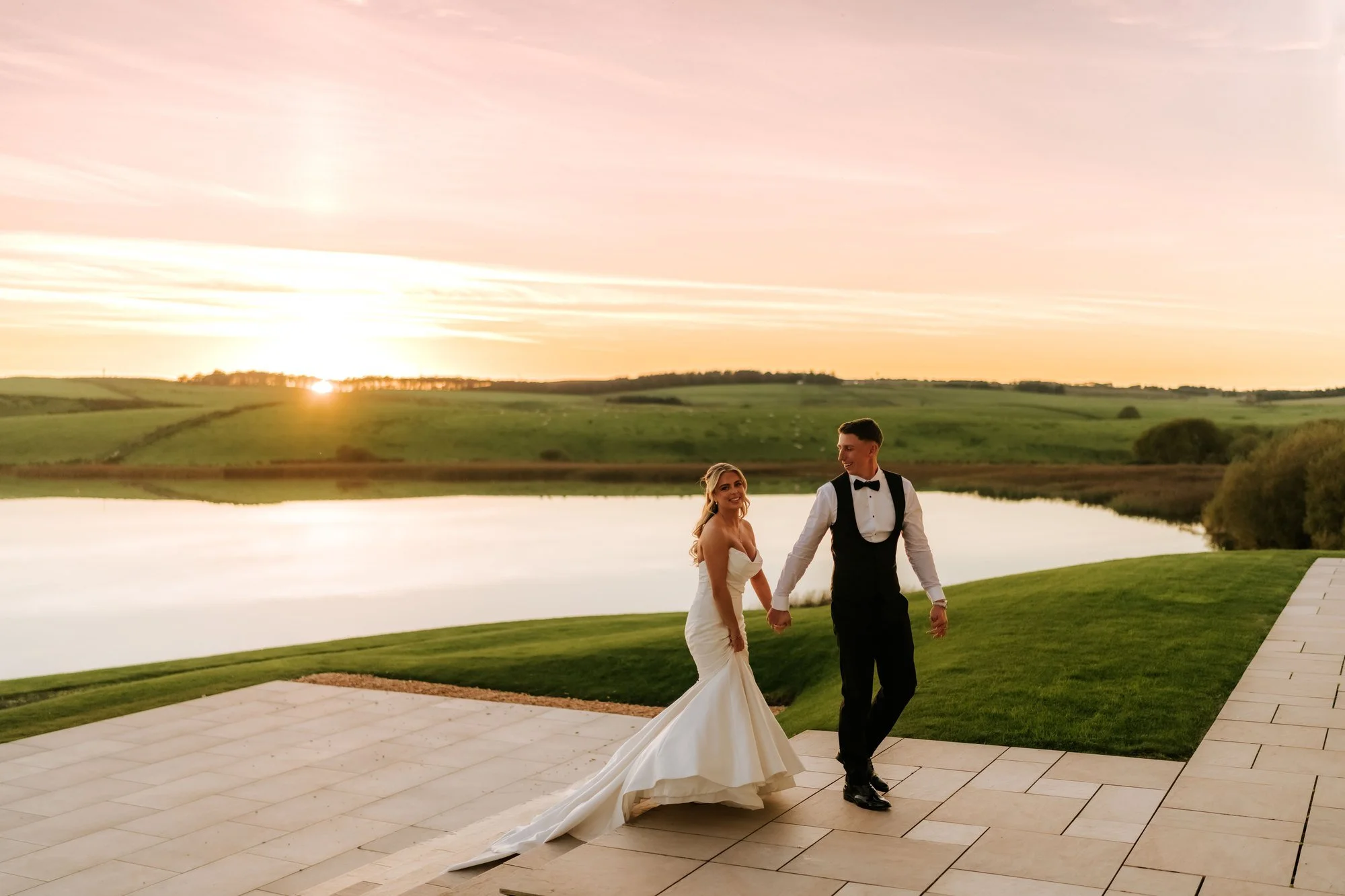Aiden and Taylor walking hand in hand beside the loch at sunset.