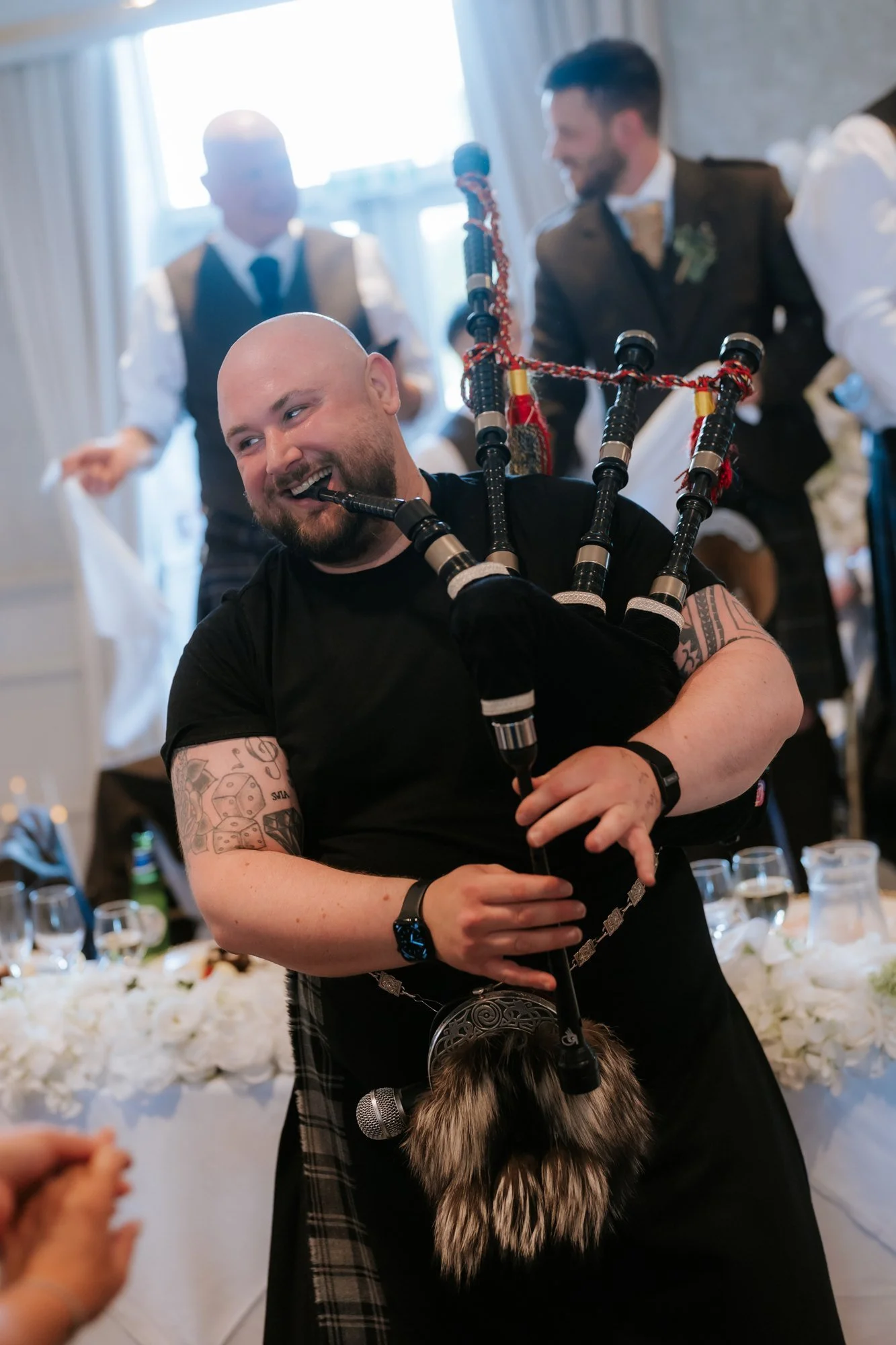 A smiling bagpiper playing among the wedding guests at Glenbervie House.