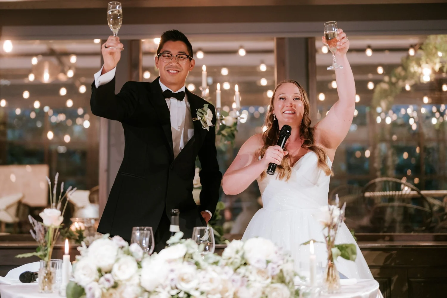 Allie holding a microphone as she and Carl raise their glasses at the wedding reception.