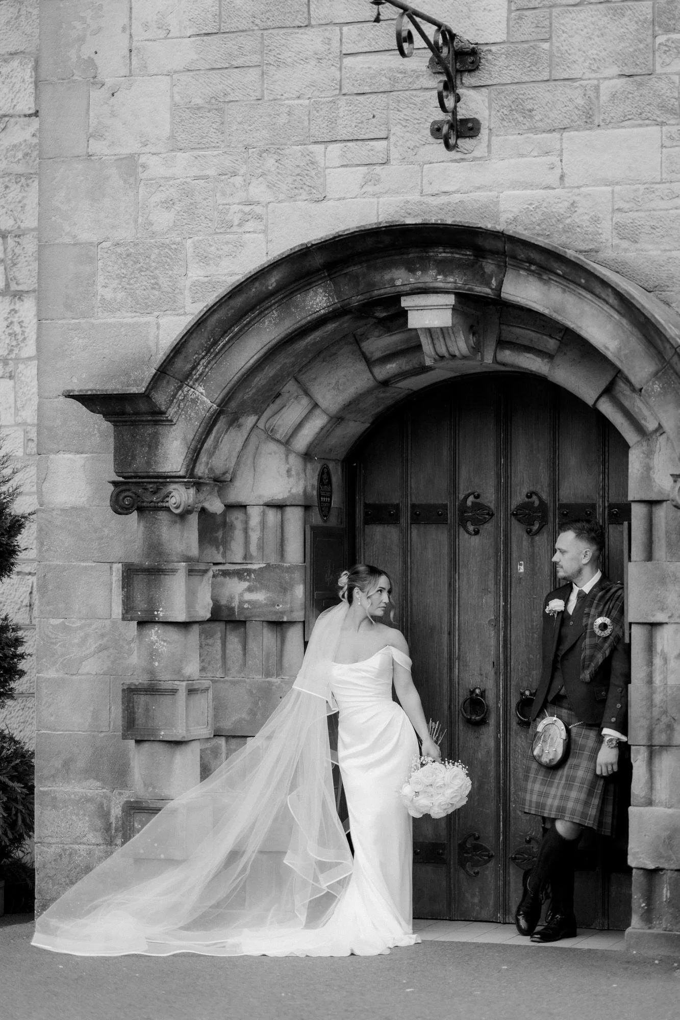 Elle and Adam standing together in a stone arched doorway