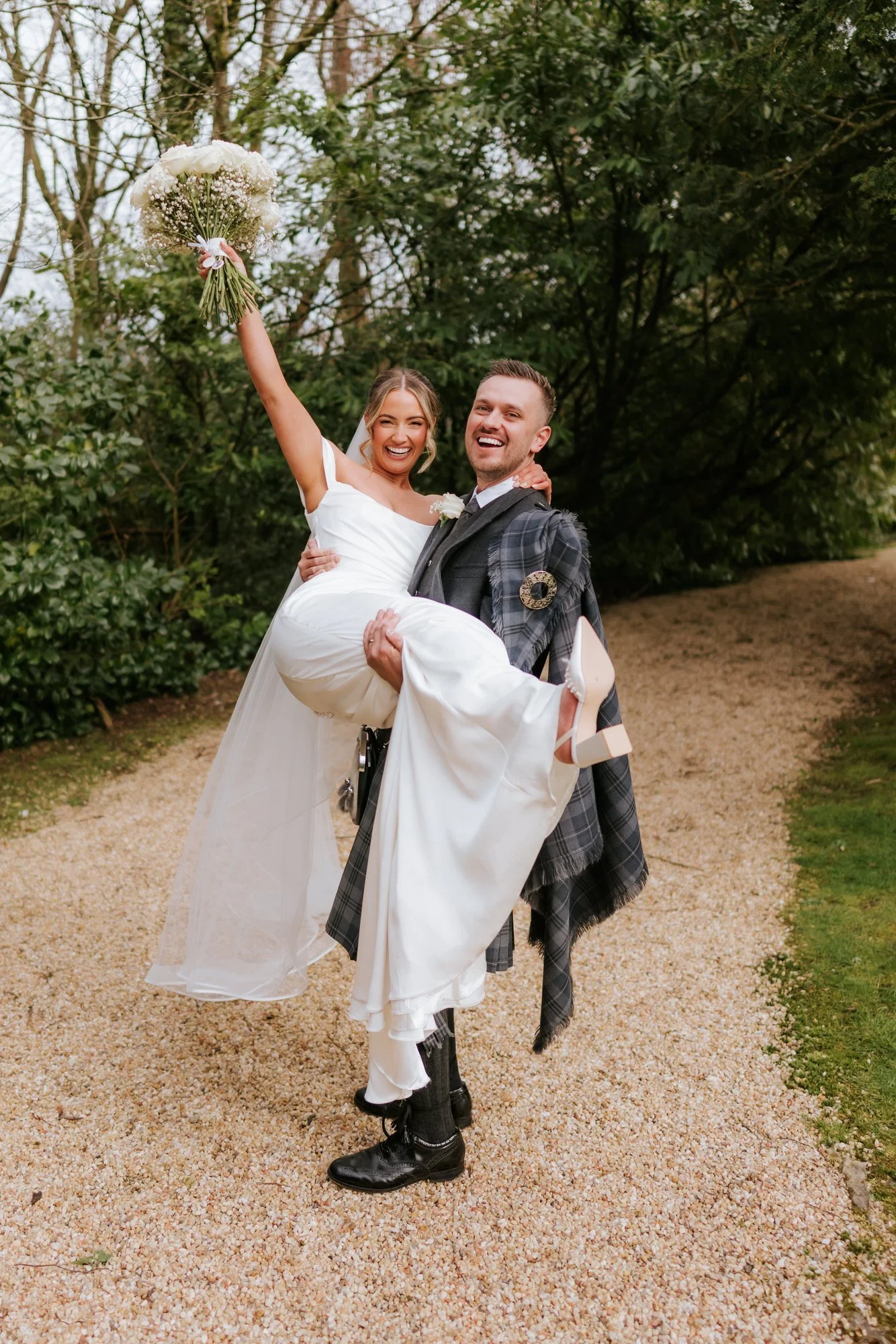Adam carrying Elle as she raises her bouquet