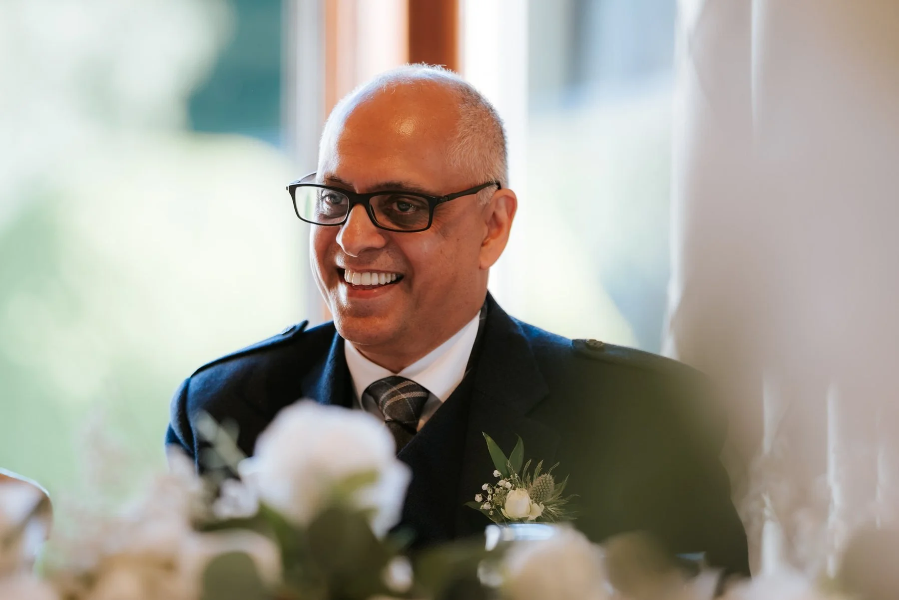 A guest in glasses smiling at the wedding reception.