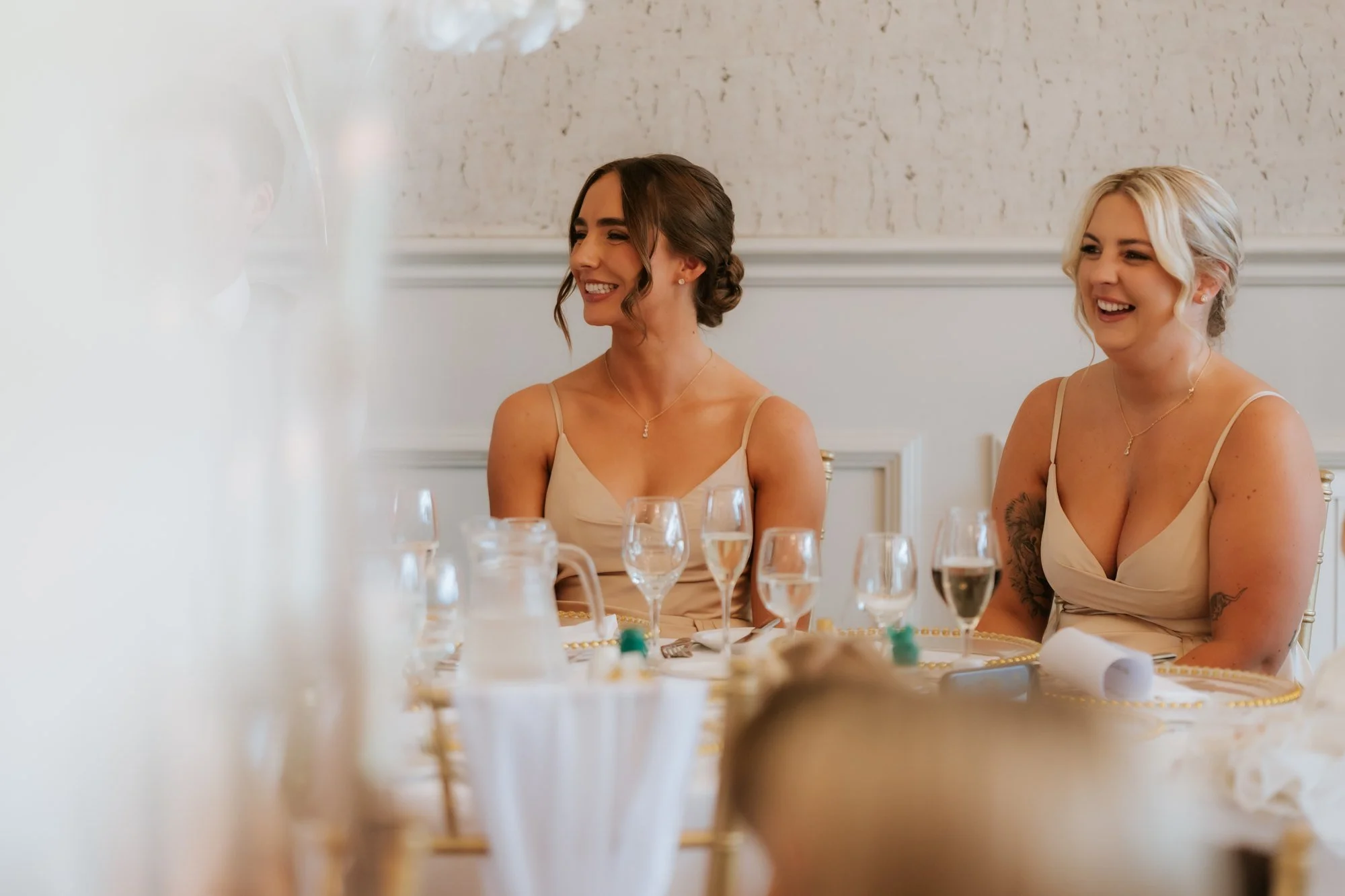Two bridesmaids in champagne-coloured dresses smiling at the top table at Glenbervie House.
