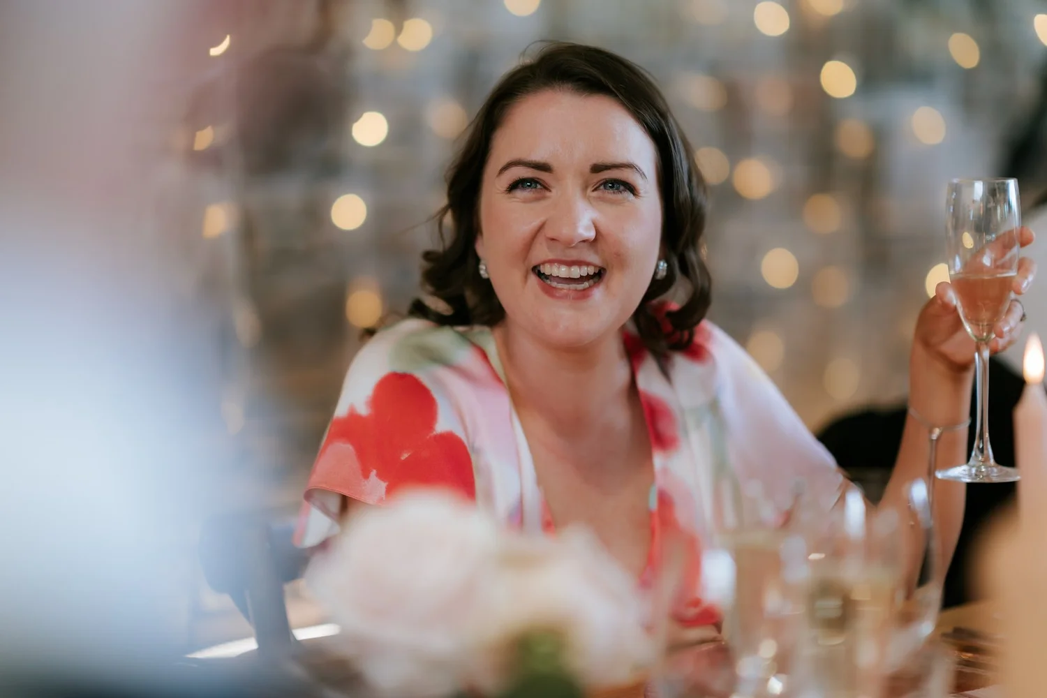 A wedding guest smiling with a glass of wine at the reception table.