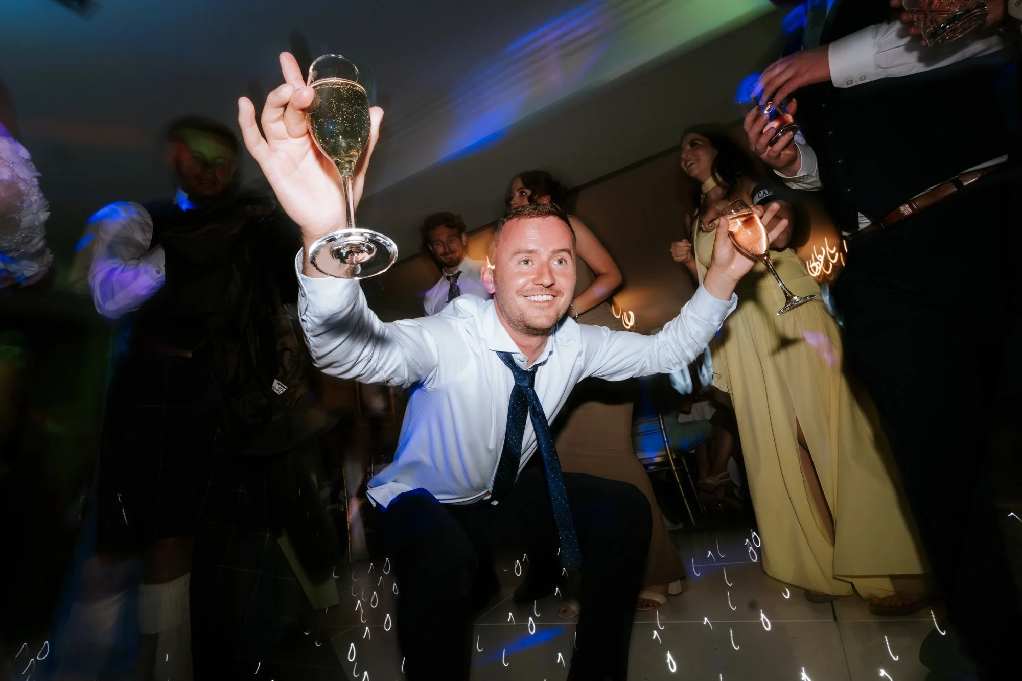 A wedding guest dancing with a raised glass in each hand at Glenbervie House.