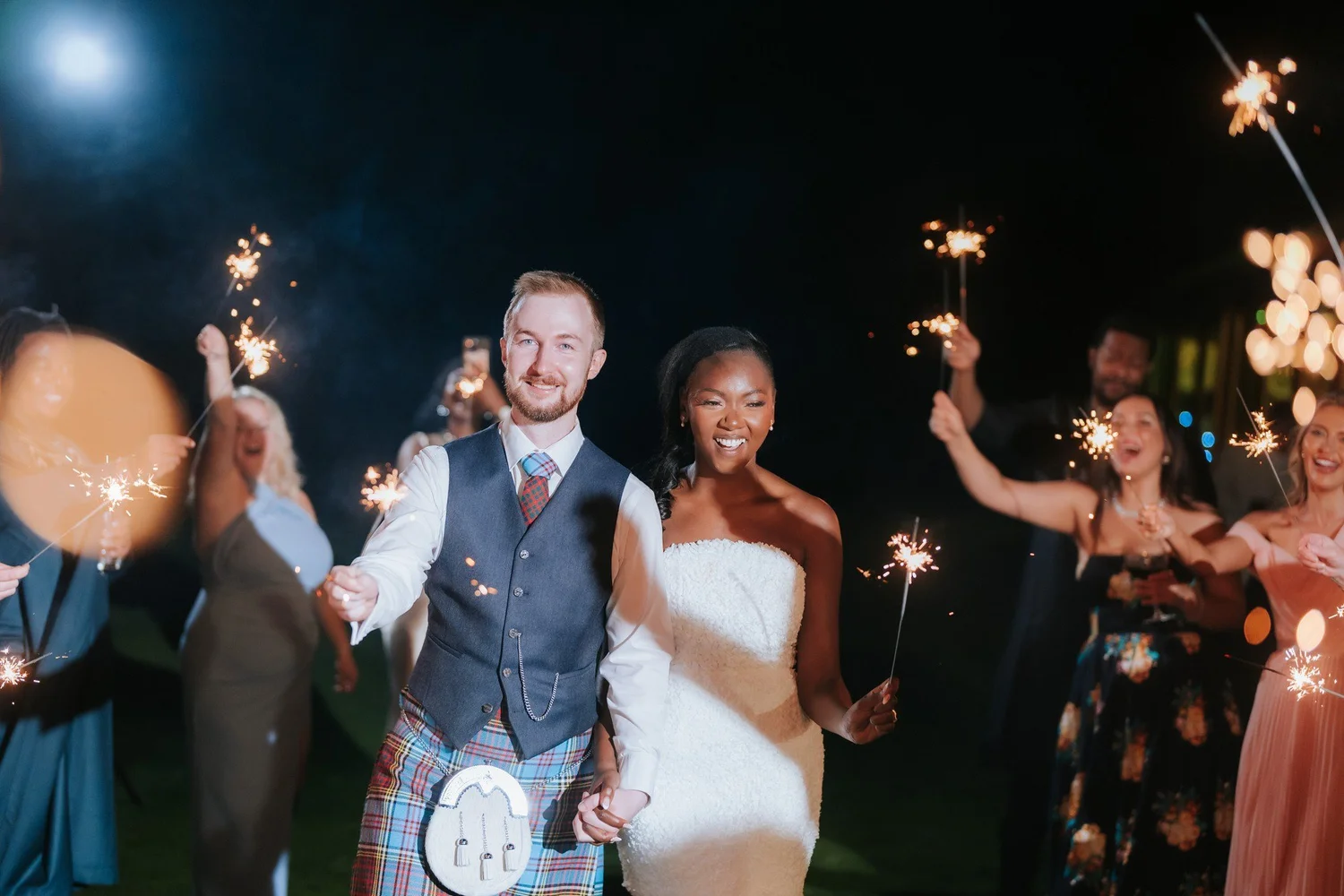 Kuda and Jamie walking hand in hand through their sparkler send-off.