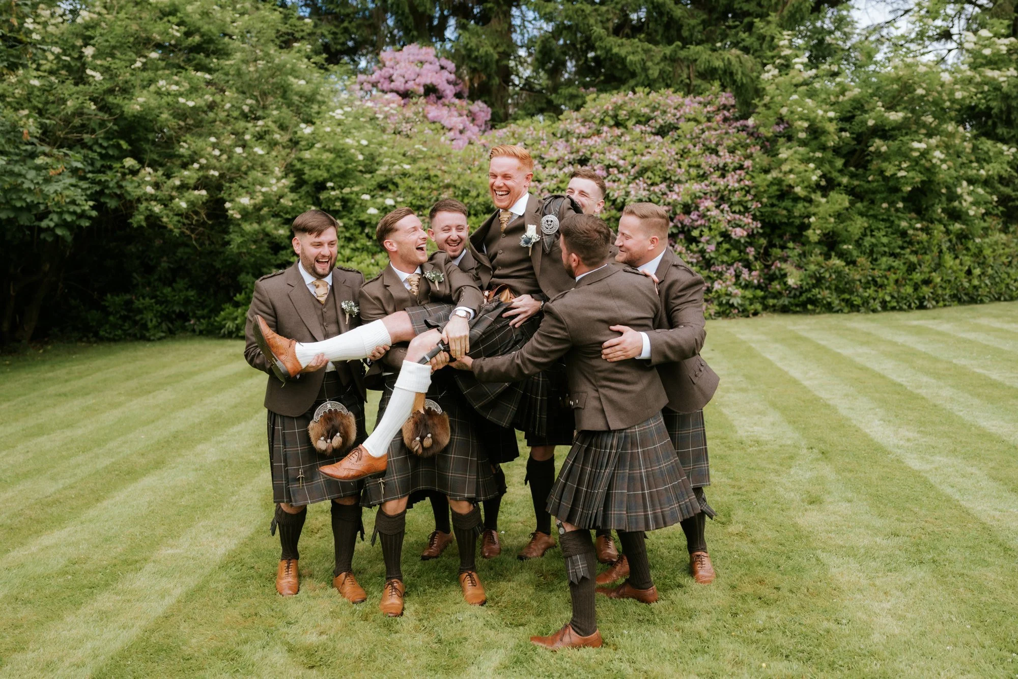 Groomsmen lifting a laughing Scott in the gardens at Glenbervie House.
