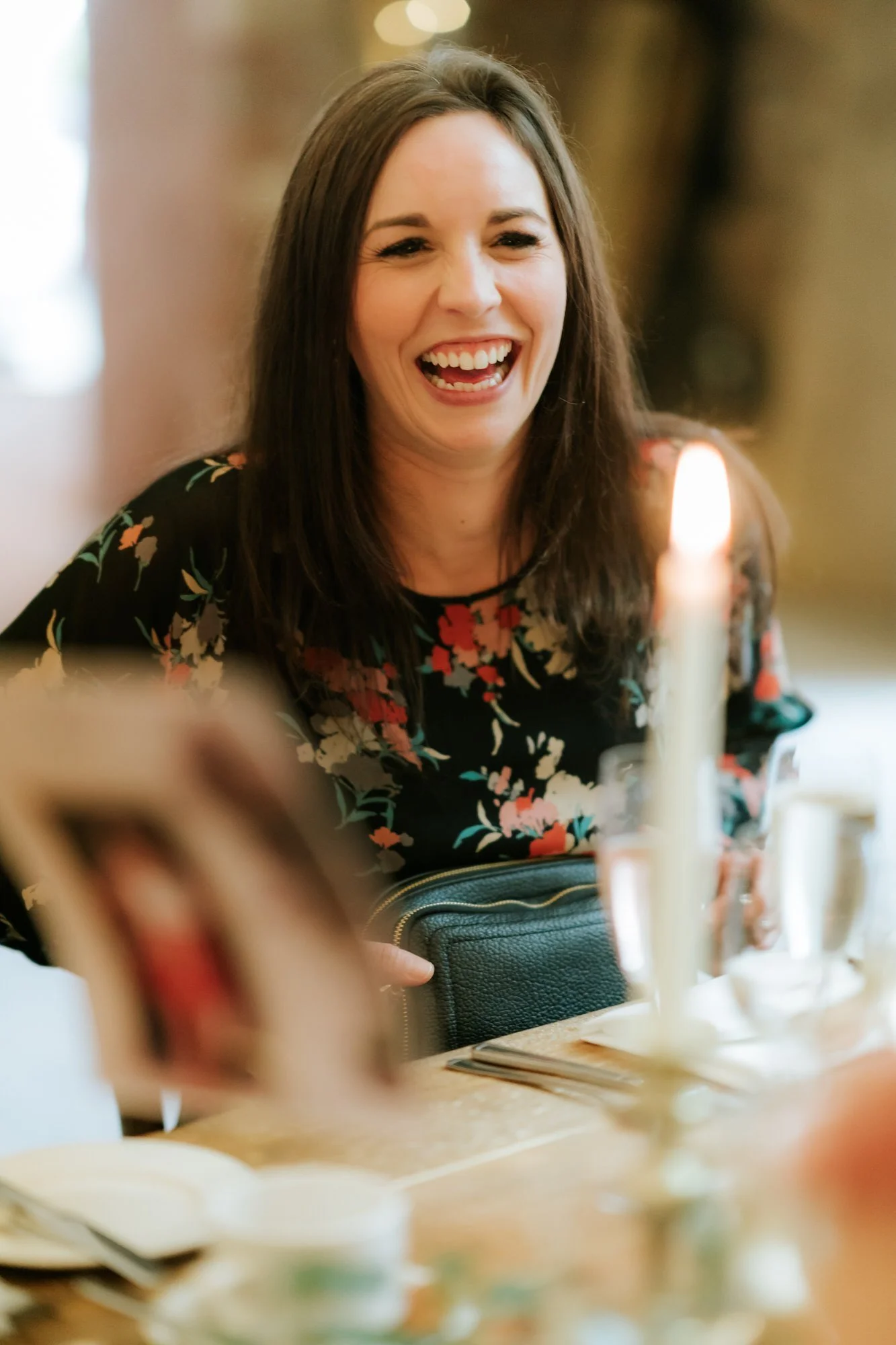 A guest in a dark floral dress laughs beside a lit taper candle at the wedding reception.