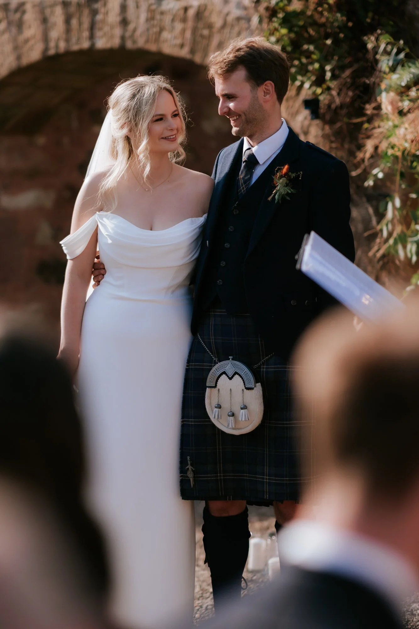 The couple stand close together in the sunshine during their courtyard wedding ceremony.