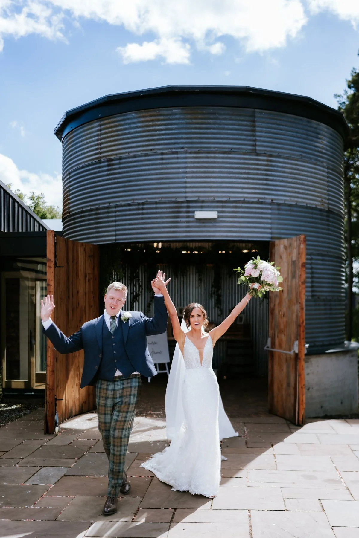 Jamie and Lauren raising their arms outside the circular silo entrance at Cairns Farm Estate.