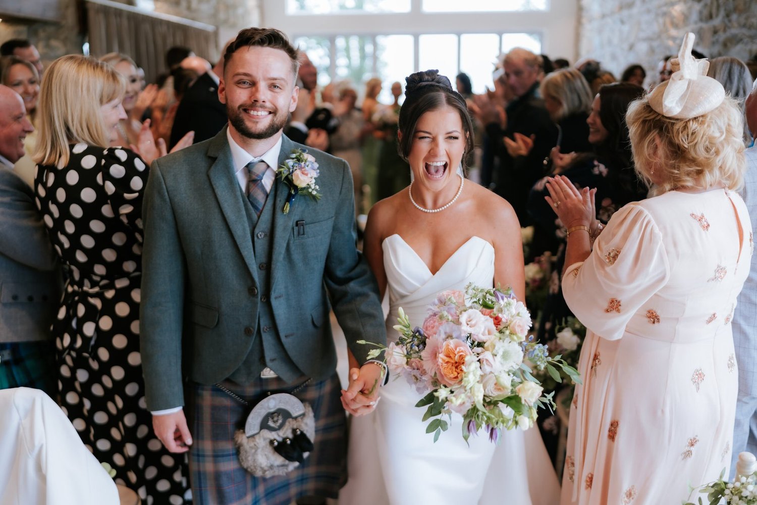 Lois laughing as she and Dougie walk back down the aisle past their cheering wedding guests.