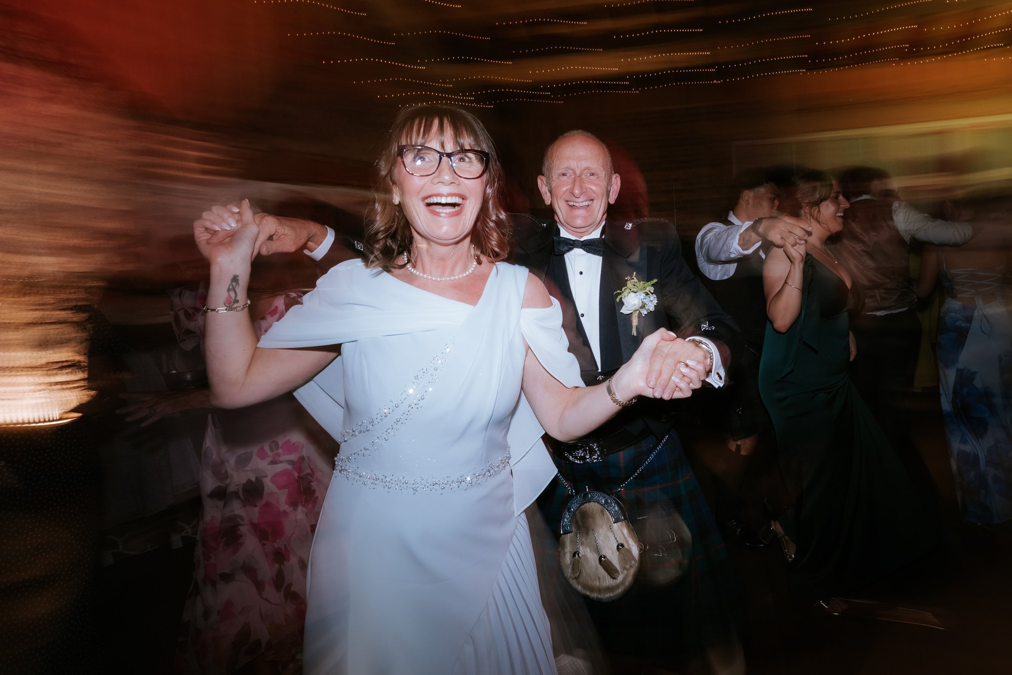 Wedding guests linking arms and dancing at the evening ceilidh.