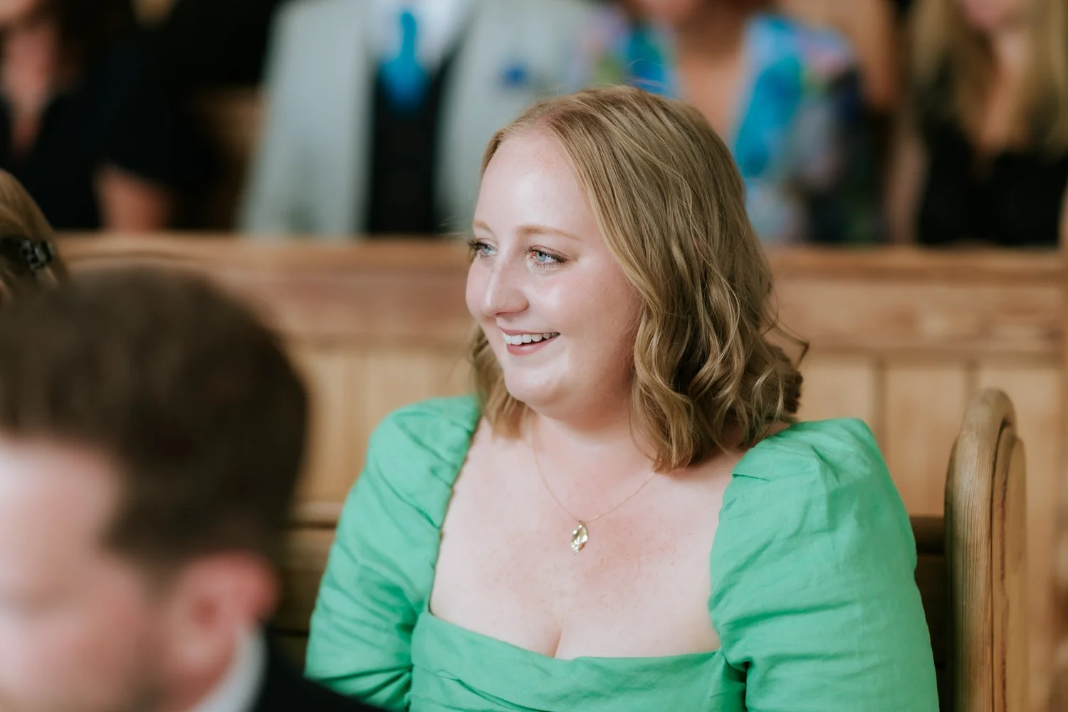 A guest in a green dress smiling during Jamie and Lauren’s ceremony.