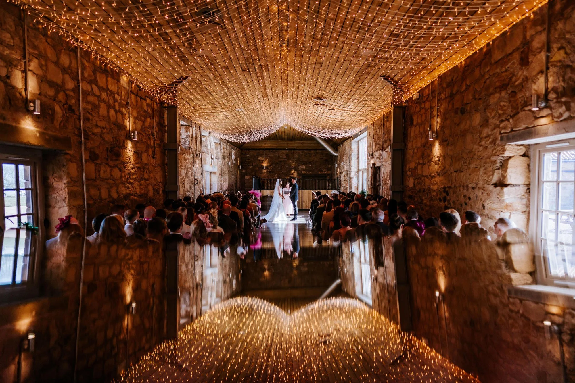 A wide view of the wedding ceremony beneath fairy lights at Falside Mill