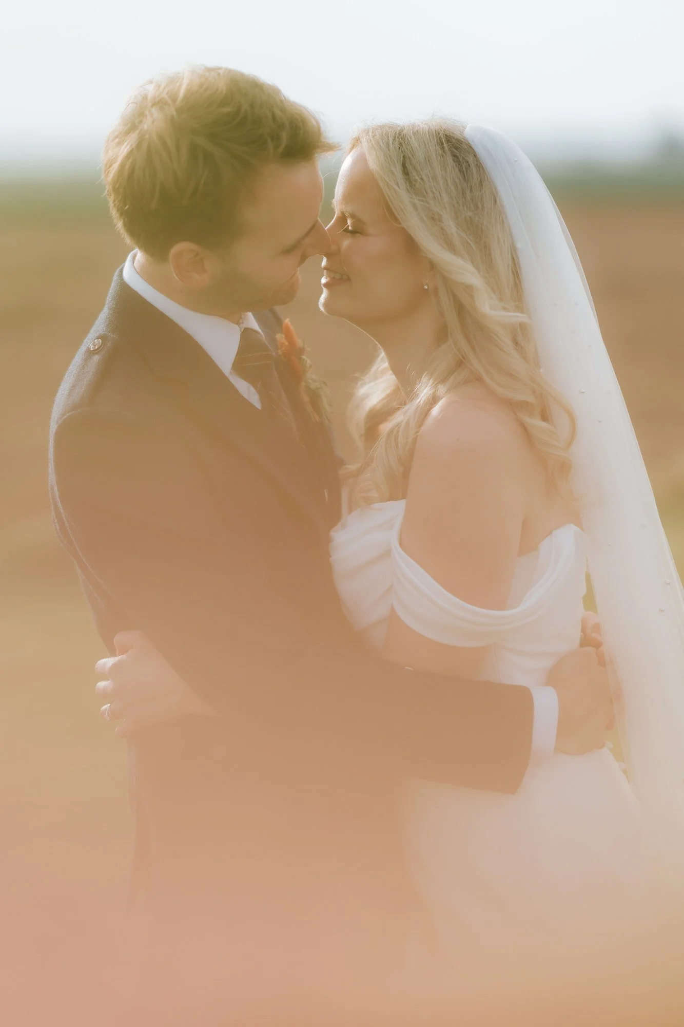 A softly framed portrait of the couple leaning close together beside the field.